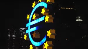 Šviečiantis euro simbolis naktiniame miesto fone, simbolizuojantis Europos centrinio banko sprendimus dėl palūkanų.