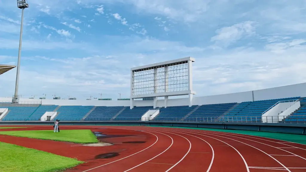 Tuščias lengvosios atletikos stadionas su raudonais bėgimo takais po giedru dangumi