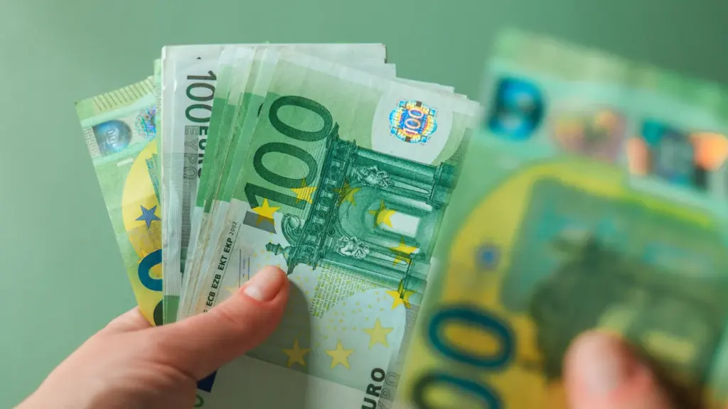 Žmogaus ranka laiko keletą žalių šimto eurų banknotų žaliame fone.