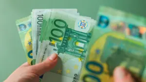 Žmogaus ranka laiko keletą žalių šimto eurų banknotų žaliame fone.
