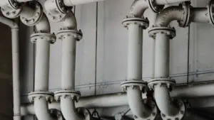 Metaliniai vamzdynai pramoninėje aplinkoje, iliustruojantys naują nuotekų tinklų infrastruktūrą Vilniaus rajone.