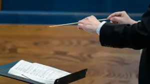 Dirigentas orkestrui vadovauja naudodamas batutą virš atverstų muzikos natų lapų.