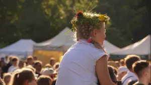 Maža mergaitė su lauko gėlių vainiku ant galvos sėdi tėčiui ant pečių minioje.