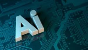 AI raidės uždėtos ant kompiuterinės mikroschemos fono simbolizuojančios dirbtinį intelektą technologijų pasaulyje.