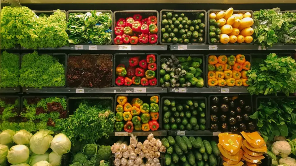 Šviežios daržovės prekybos centro lentynose, iliustruojančios maisto produktų kainų pokyčius ir PVM lengvatas.