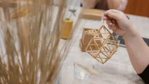 Moteris laiko rankoje iš šiaudų surištą geometrinį tradicinį lietuvišką Kalėdų papuošalą sodą.